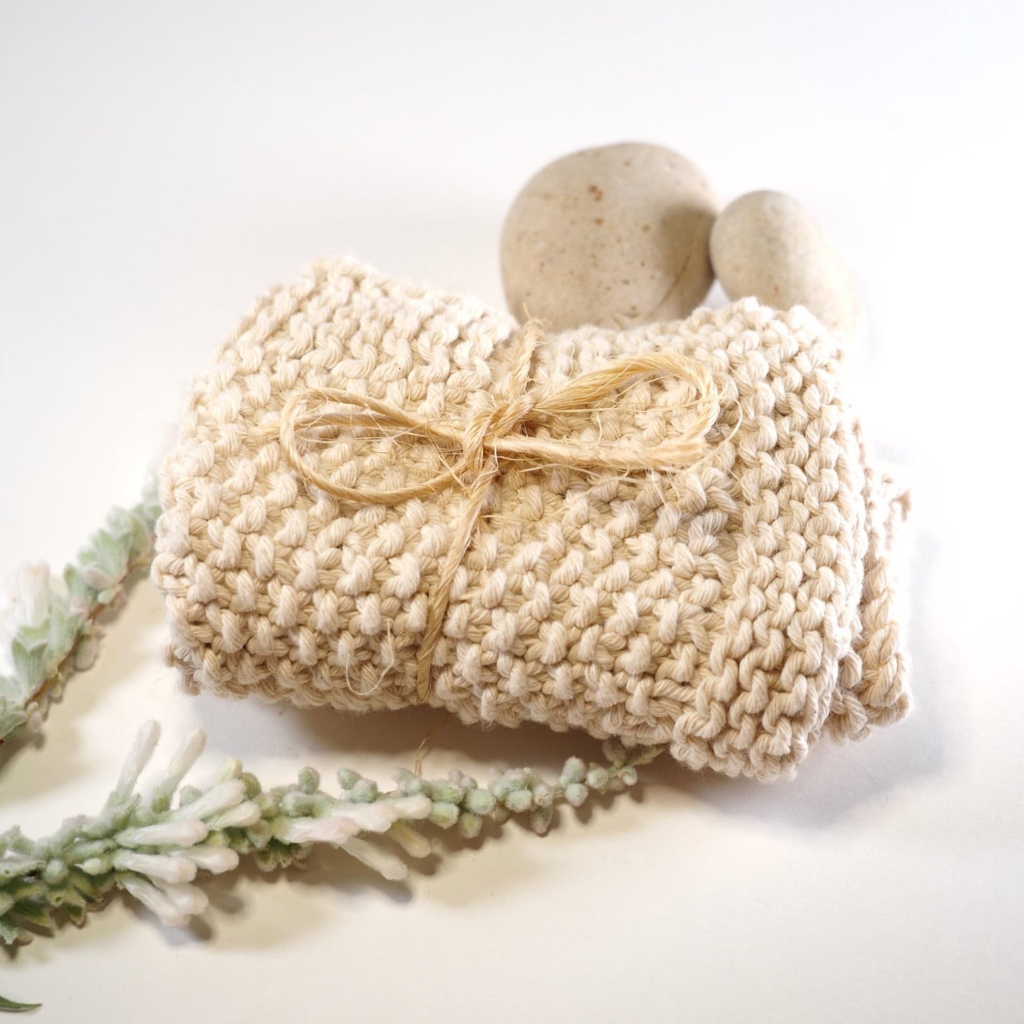 Hand knitted cotton face cloth folded with rock and flower