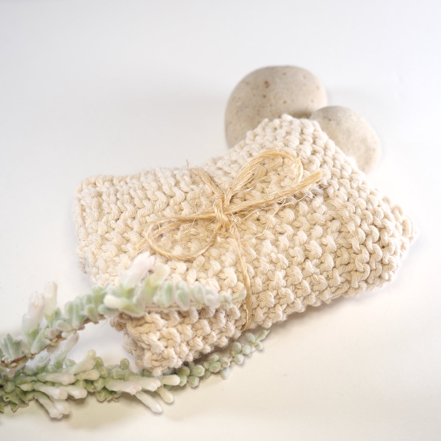 Hand knitted cotton face cloth folded and tied with string with rock and flower.