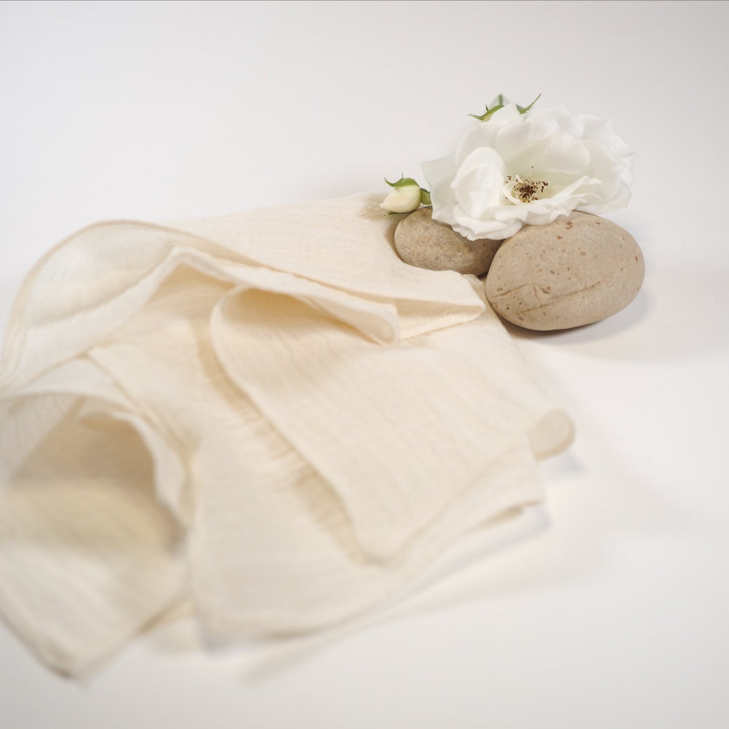 Handmade organic cotton muslin facecloth softly folded with rose and rock.