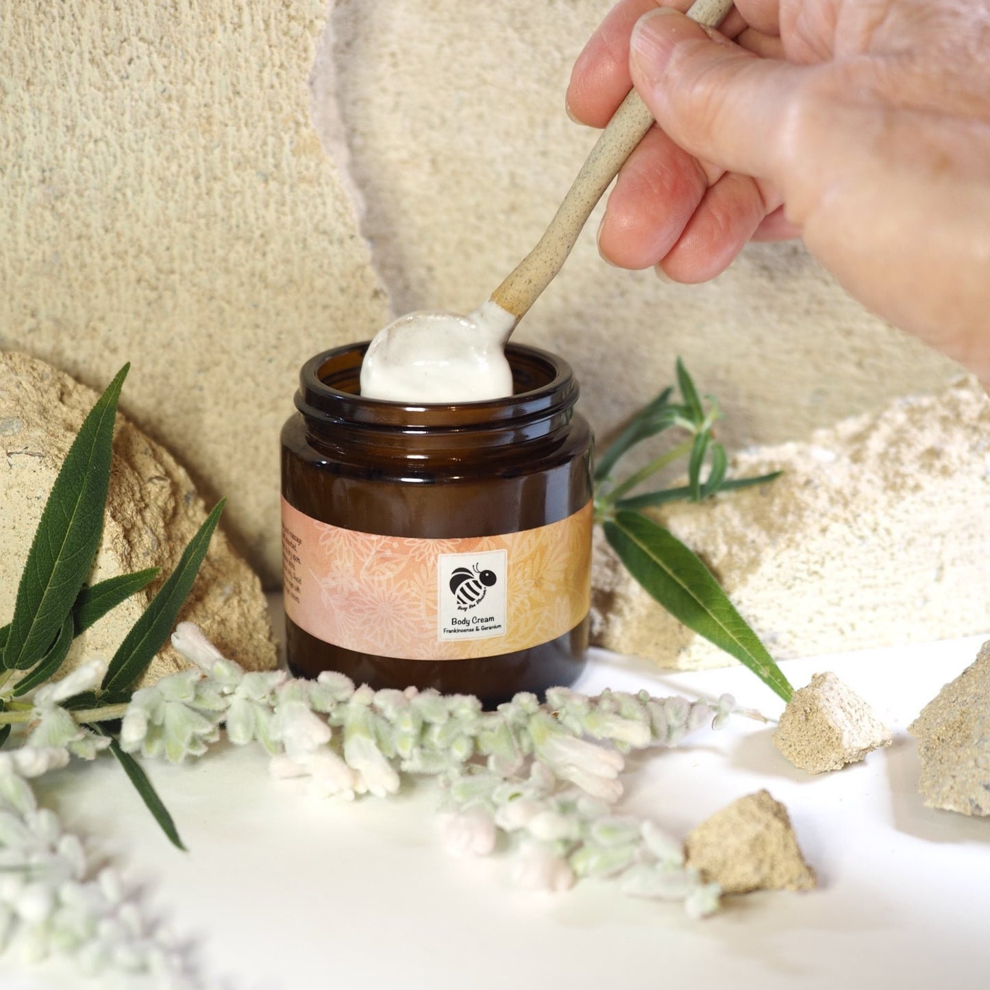 Frankincense and Geranium Body Cream with hands holding ceramic spoon in cream