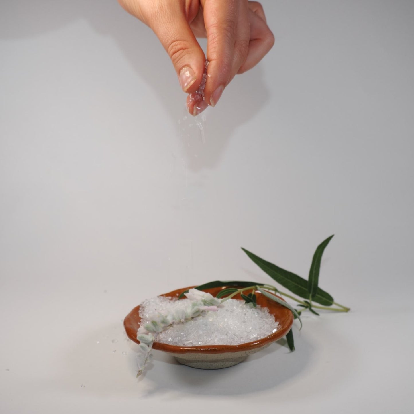 Sweet Orange Blossom Bath Soak with hands sprinkling Epsom Salts into a ceramic dish.