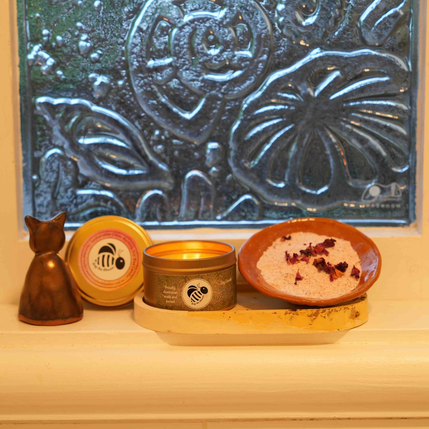 Bathroom windowsill with a lit candle, candle snuffer and Goat ate my roses Milk Bath Soak