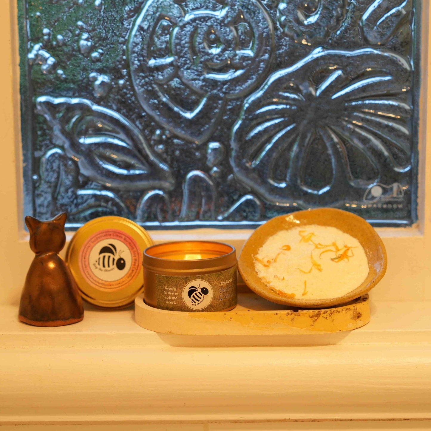 Bergamot and Banksia travel tin candle lit with Candle snuffer and Lemon Calendula Milk Bath Soak on bathroom window sill