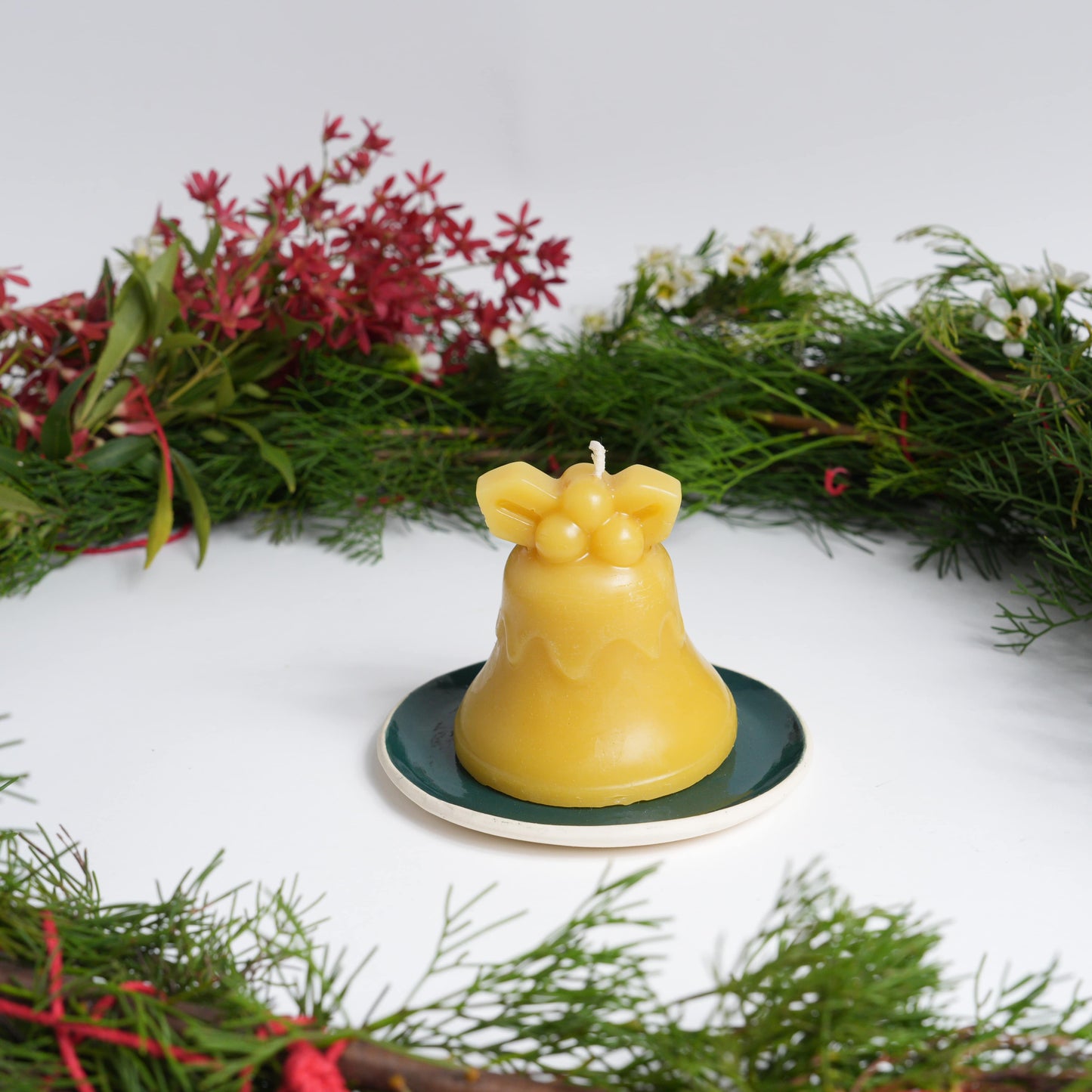 Chrismas bell beeswax candle on green plate with Christmas wreath