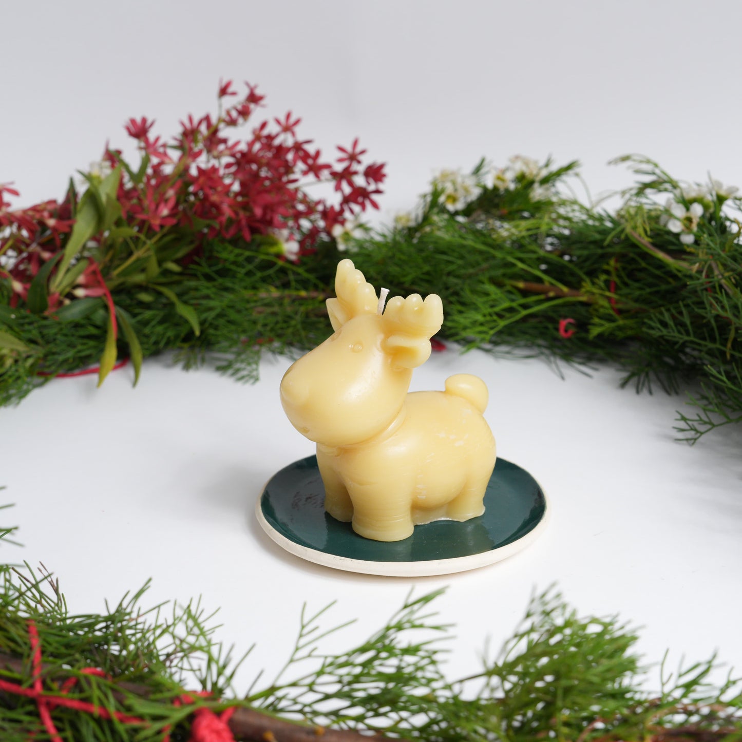 Rudolph beeswax candle for Christmas on a green ceramic plate with Christmas wreath