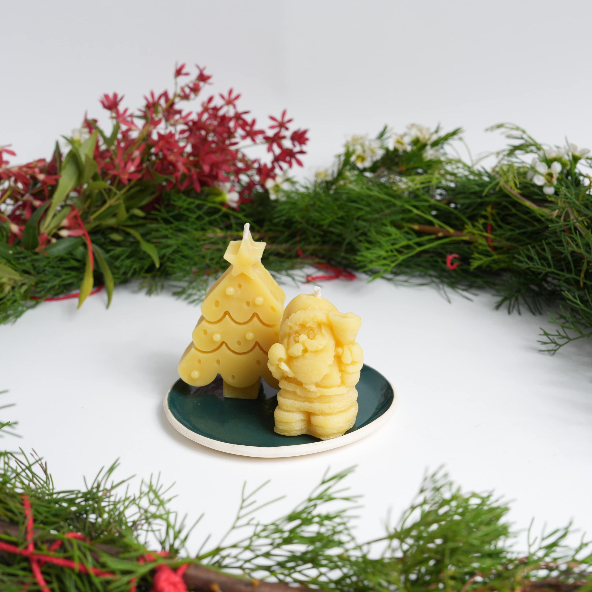 Santa and Christmas tree beeswax candles on a green ceramic plate with wreath