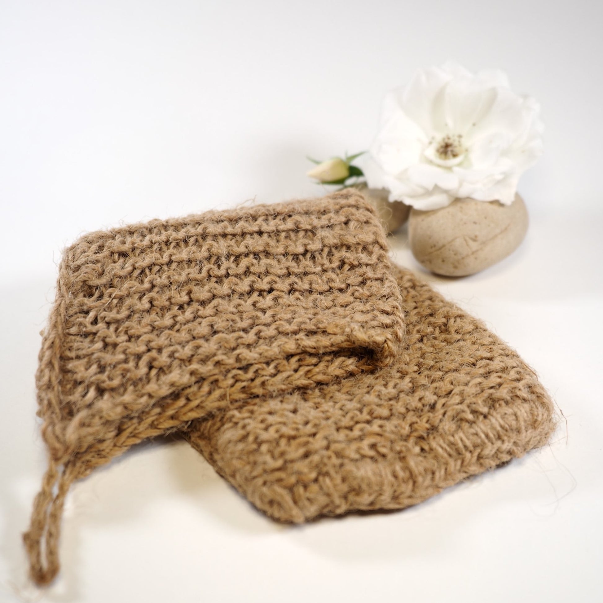 Hand crocheted jute exfoliating mitt folded with rock and rose